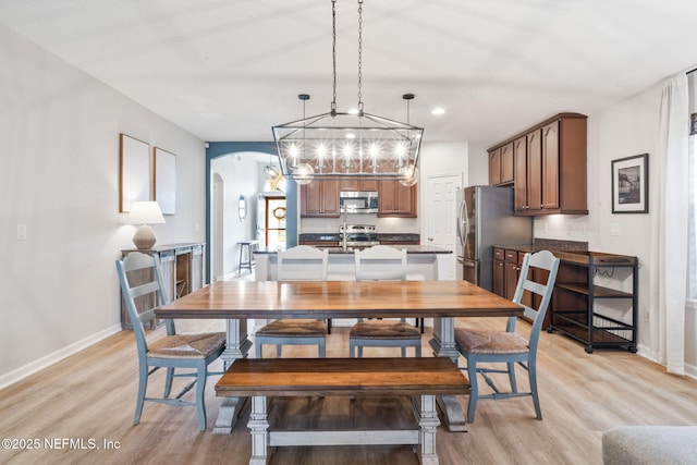 dining space featuring recessed lighting, arched walkways, light wood-type flooring, and baseboards