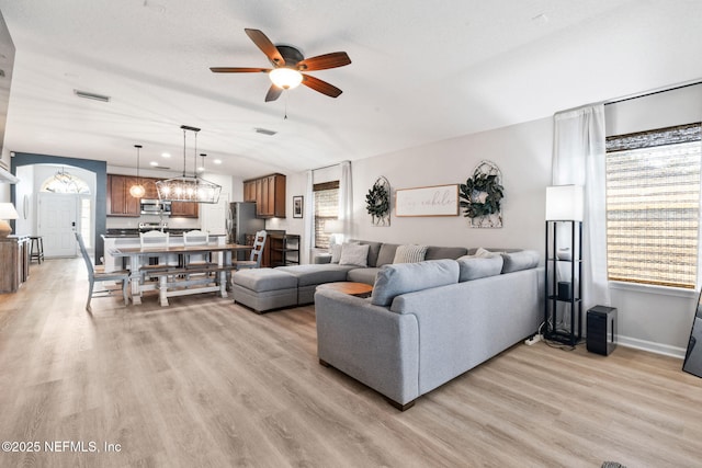 living area with a wealth of natural light, light wood-style floors, ceiling fan with notable chandelier, and baseboards