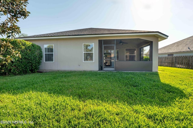 rear view of house with a sunroom, a yard, ceiling fan, fence, and stucco siding
