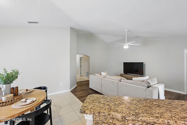 tiled living area with visible vents, a ceiling fan, arched walkways, and lofted ceiling