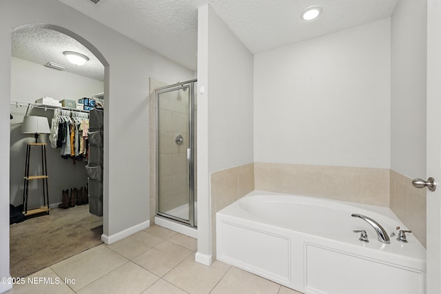 full bathroom with a bath, a textured ceiling, a walk in closet, tile patterned floors, and a stall shower