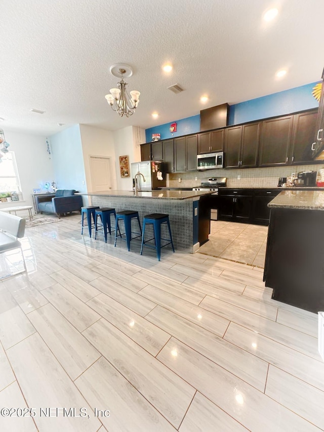 kitchen featuring decorative backsplash, a notable chandelier, a breakfast bar, visible vents, and appliances with stainless steel finishes