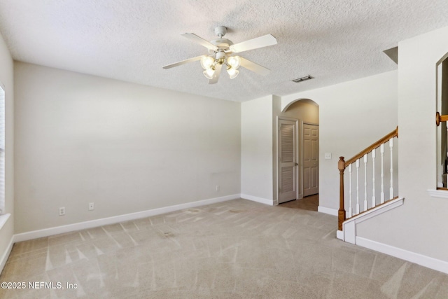 empty room featuring stairway, visible vents, arched walkways, carpet flooring, and ceiling fan