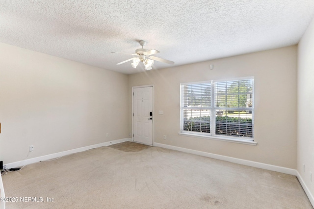 empty room with light carpet, a ceiling fan, a textured ceiling, and baseboards