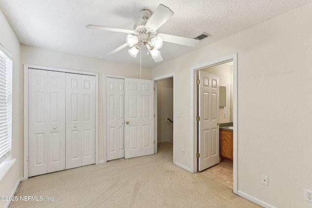 unfurnished bedroom featuring multiple closets, visible vents, baseboards, and light carpet