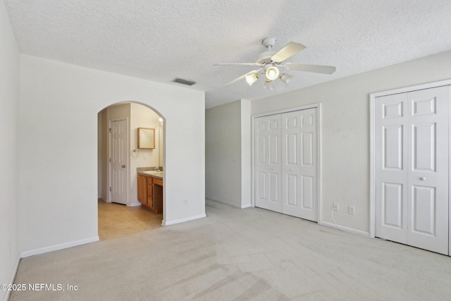 unfurnished bedroom featuring multiple closets, visible vents, light carpet, arched walkways, and a textured ceiling