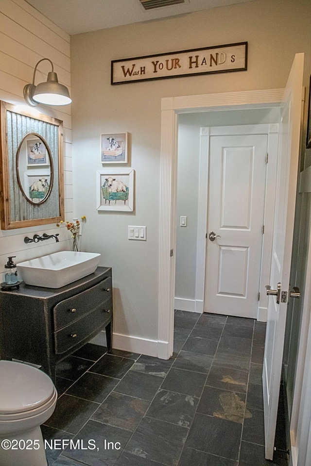 bathroom with baseboards, toilet, vanity, and visible vents