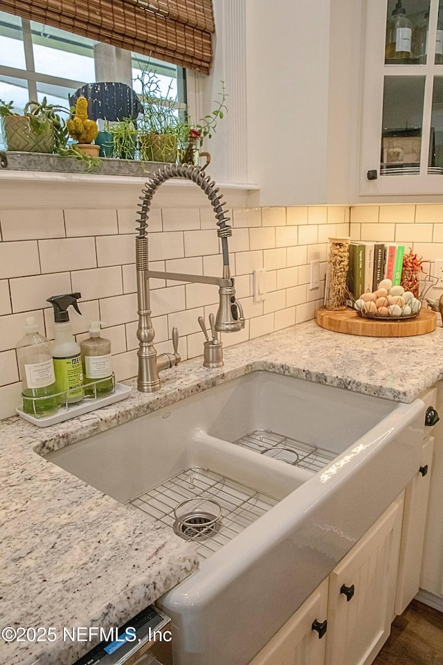 details with white cabinets, backsplash, a sink, light stone countertops, and glass insert cabinets