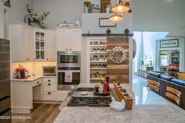 kitchen with light stone counters, glass insert cabinets, dark wood finished floors, backsplash, and appliances with stainless steel finishes
