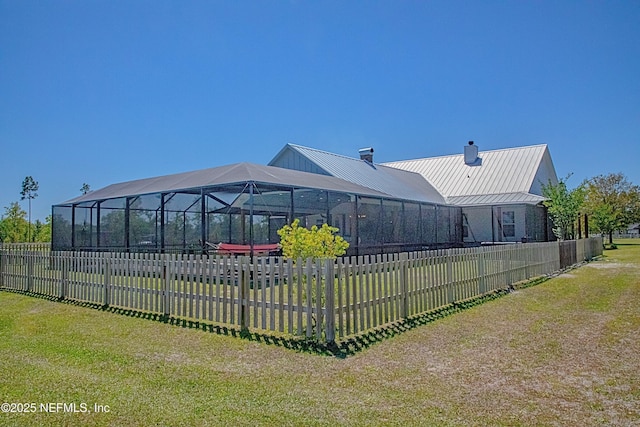 rear view of property featuring a chimney, glass enclosure, a fenced backyard, and metal roof