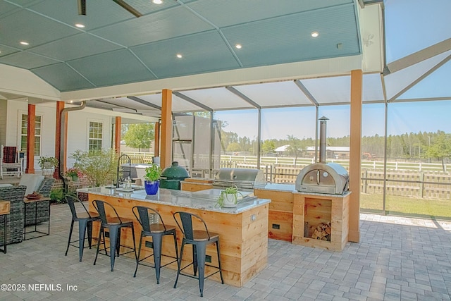 view of patio / terrace featuring exterior kitchen, fence, grilling area, a lanai, and outdoor wet bar