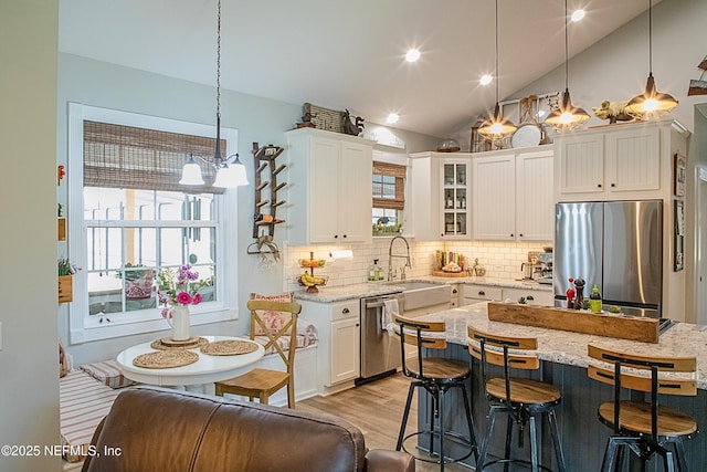 kitchen with white cabinets, vaulted ceiling, a notable chandelier, a breakfast bar, and appliances with stainless steel finishes