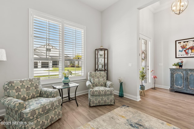 sitting room featuring an inviting chandelier, baseboards, wood finished floors, and a towering ceiling