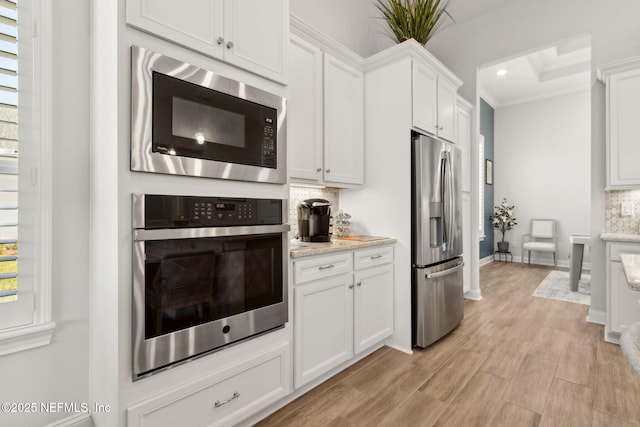 kitchen featuring decorative backsplash, crown molding, light stone countertops, stainless steel appliances, and white cabinetry