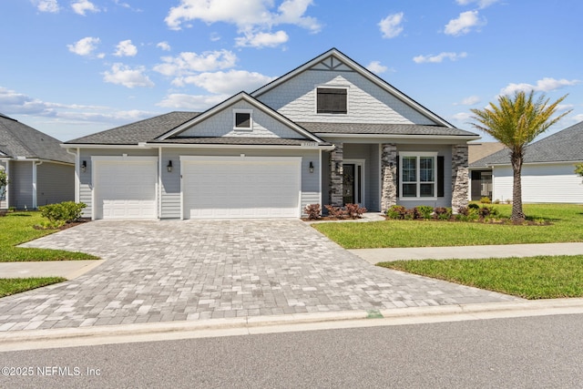 craftsman-style house with an attached garage, decorative driveway, a front lawn, and stone siding