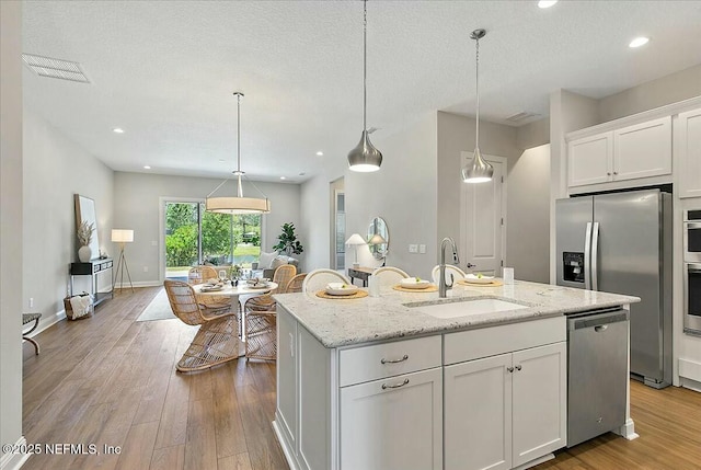 kitchen featuring hanging light fixtures, a sink, appliances with stainless steel finishes, an island with sink, and white cabinetry