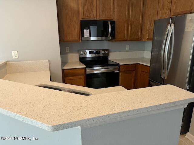 12301 Kernan Forest Blvd Unit 302, Jacksonville, FL 32225 - kitchen featuring brown cabinets, stainless steel appliances, and light stone counters