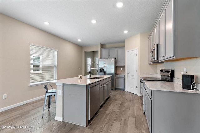 2176 Major Oak St, Jacksonville, FL 32218 - kitchen featuring a kitchen island with sink, light wood-style flooring, a breakfast bar area, appliances with stainless steel finishes, and gray cabinetry