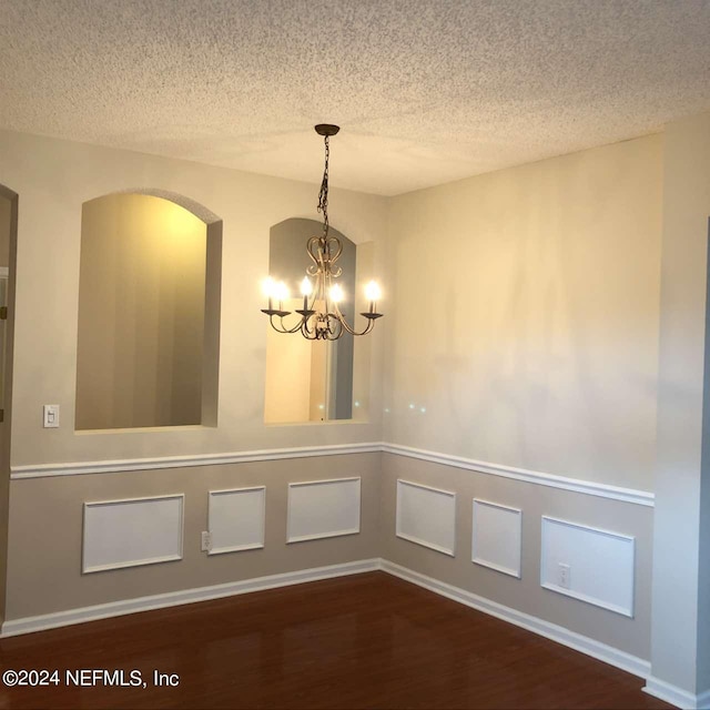 unfurnished dining area with wood finished floors, an inviting chandelier, a textured ceiling, and arched walkways