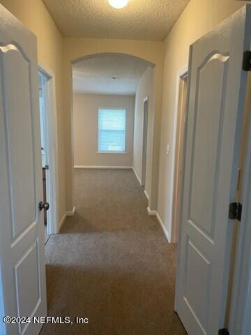 corridor featuring dark colored carpet, a textured ceiling, baseboards, and arched walkways