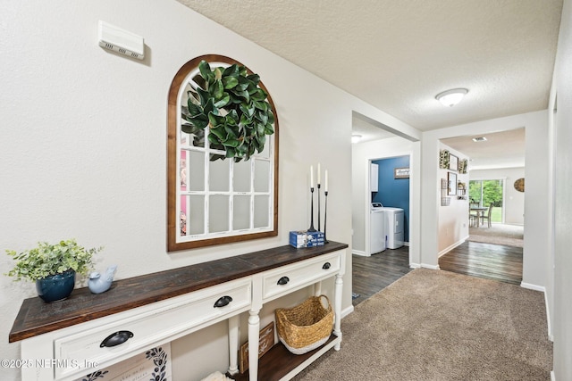 hallway featuring separate washer and dryer, a textured ceiling, baseboards, and dark colored carpet