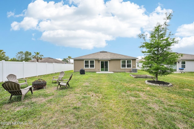 rear view of house with a lawn, central AC, fence, a fire pit, and stucco siding