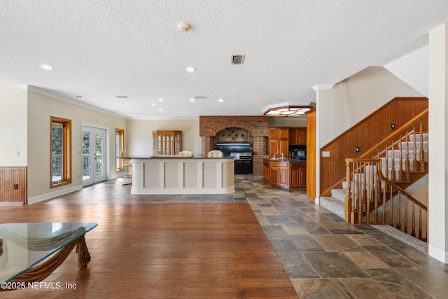 kitchen featuring a textured ceiling, open floor plan, visible vents, brown cabinets, and an island with sink