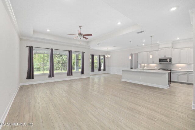 121 Oxford Estates Way, Saint Johns, FL 32259 - unfurnished living room featuring visible vents, ceiling fan with notable chandelier, light wood-style flooring, and a tray ceiling