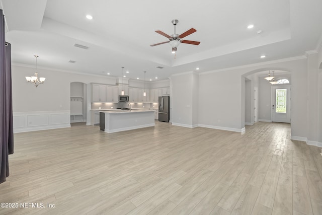 121 Oxford Estates Way, Saint Johns, FL 32259 - unfurnished living room featuring light wood-type flooring, arched walkways, a raised ceiling, and ceiling fan with notable chandelier