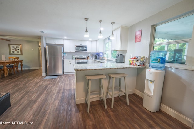 kitchen with dark wood-type flooring, a peninsula, appliances with stainless steel finishes, and baseboards