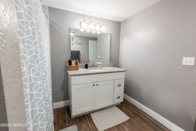 bathroom featuring a textured wall, baseboards, vanity, and wood finished floors