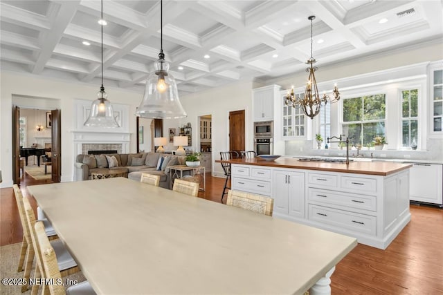 dining room with a notable chandelier, a fireplace, beamed ceiling, coffered ceiling, and wood finished floors