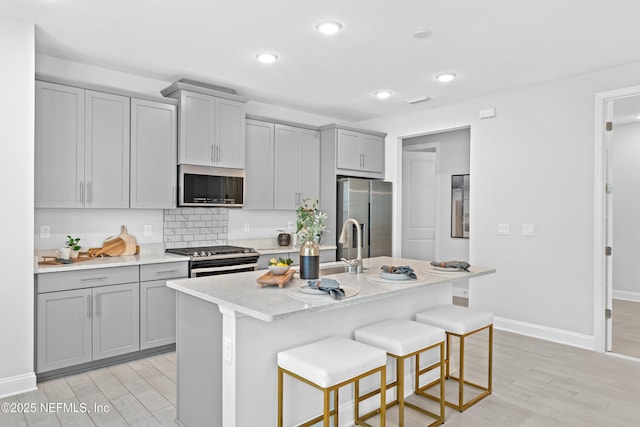 130 Juniper Hills Dr, Saint Johns, FL 32259 - kitchen with stainless steel appliances, gray cabinetry, light wood-style flooring, a kitchen breakfast bar, and an island with sink