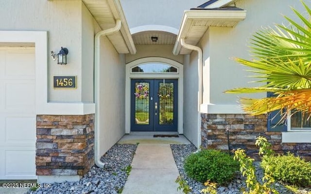 entrance to property with french doors, stone siding, a garage, and stucco siding