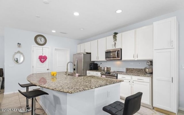 kitchen with a sink, a kitchen bar, white cabinetry, a center island with sink, and stainless steel appliances