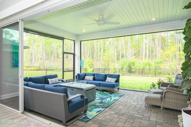 sunroom featuring a forest view, ceiling fan, and an outdoor living space with a fire pit
