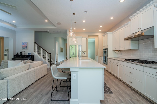 kitchen featuring a breakfast bar, open floor plan, under cabinet range hood, a sink, and stainless steel appliances
