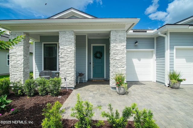 doorway to property featuring a porch, decorative driveway, an attached garage, and stone siding