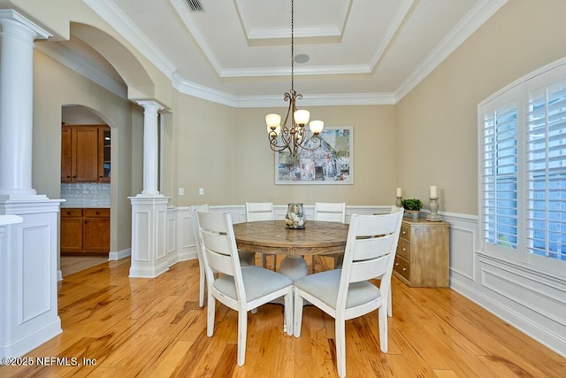 dining space with a tray ceiling, light wood-style floors, arched walkways, and ornate columns