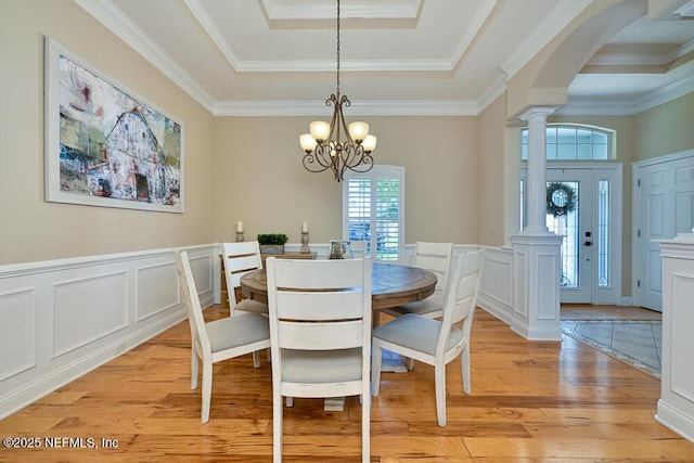 dining room with light wood-style flooring, a tray ceiling, decorative columns, and a healthy amount of sunlight