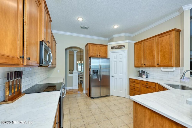 kitchen featuring stainless steel appliances, a sink, visible vents, ornate columns, and brown cabinetry