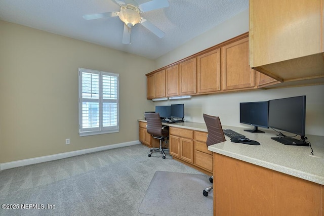 office space featuring light colored carpet, ceiling fan, baseboards, and built in desk