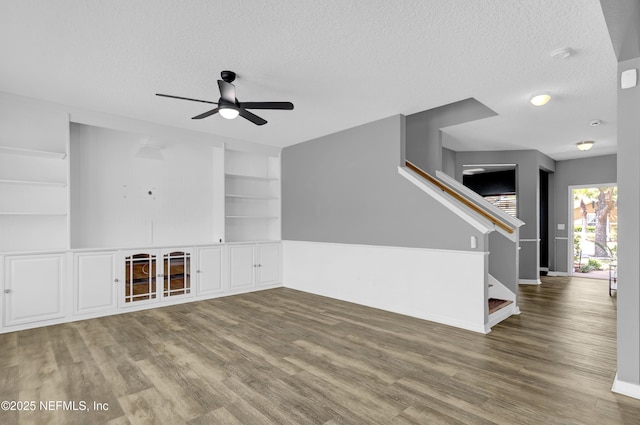 unfurnished living room featuring stairway, a ceiling fan, wood finished floors, and a textured ceiling