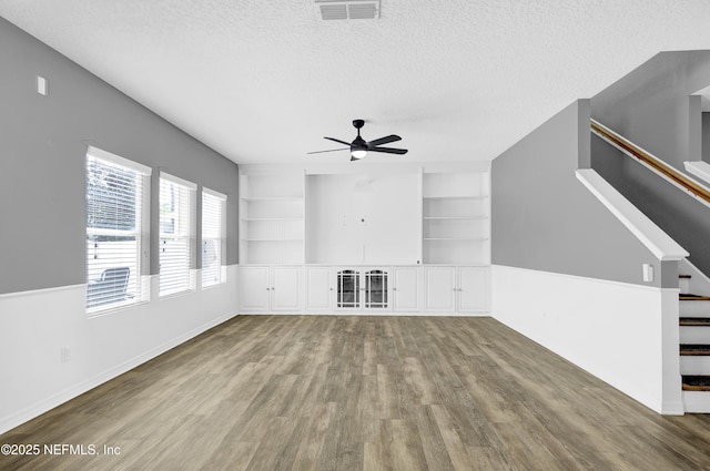 unfurnished living room with a textured ceiling, stairs, visible vents, ceiling fan, and wood finished floors