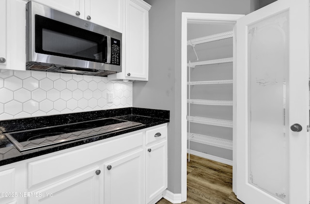 kitchen with stainless steel microwave, white cabinetry, black electric stovetop, and backsplash