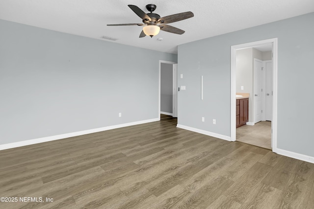unfurnished bedroom featuring visible vents, baseboards, ensuite bath, and wood finished floors