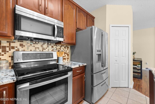 7250 Deerfoot Point Cir Unit 1, Jacksonville, FL 32256 - kitchen featuring light stone countertops, light tile patterned flooring, stainless steel appliances, brown cabinets, and backsplash