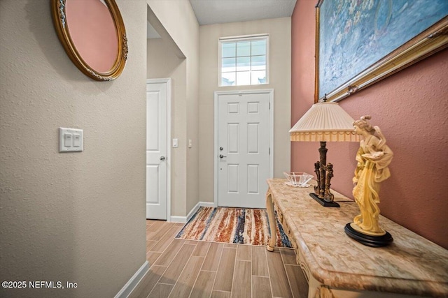 foyer with baseboards, a textured wall, and wood finished floors