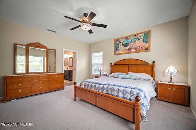 carpeted bedroom featuring a ceiling fan, baseboards, visible vents, and ensuite bath