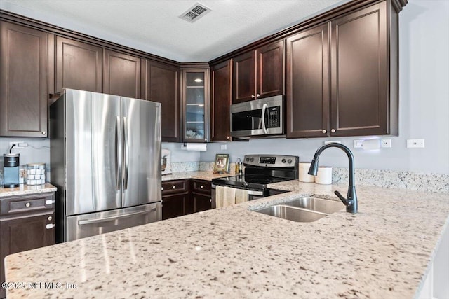 1580 Landau Rd, Jacksonville, FL 32225 - kitchen featuring stainless steel appliances, a sink, dark brown cabinets, light stone counters, and glass insert cabinets